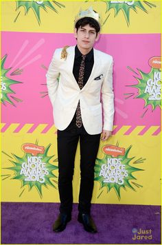 a young man in a suit and tie standing on the purple carpet at an awards event