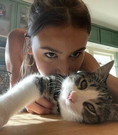 a woman laying on top of a wooden table next to a gray and white cat