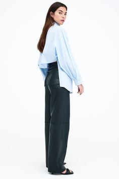 Our Ezra Shirt is a capsule wardrobe dream for your closet. Crafted from 100% crisp European poplin cotton, she offers a classic button-up silhouette in front, but with a cropped back for modern edge. Say hello, as well, to her diagonal seams at the front, sleek collar and long dolman sleeves finished with mother-of-pearl button cuffs. Wear Ezra tucked, tied or open and free—she never fails to inspire new looks.[SPLIT] Rocio, in light blue and in black, is 5'9.5" (175 cm) tall, wearing size XS. Fall Poplin Shirt For Workwear, Chic Poplin Button-up Shirt, Fall Workwear Poplin Shirt, Fall Workwear Poplin Tops, Casual Poplin Blouse For Workwear, Chic Oversized Tops For Business Casual, Oversized Blouse For Business Casual In Spring, Chic Poplin Shirt For Daywear, Modern Cropped Cotton Shirt For Work