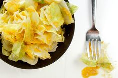 a black plate topped with lettuce and cheese next to a fork on a white table