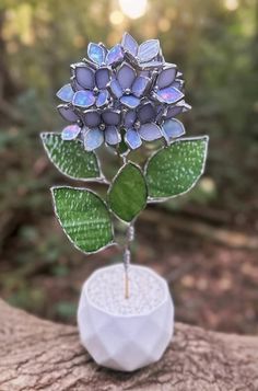 a silver brooch with blue flowers and green leaves on it sitting on a piece of wood