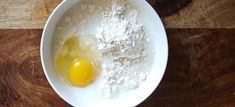 an egg and flour in a bowl on a wooden table