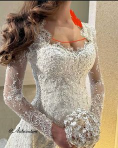 a woman in a white wedding dress with long sleeves and an orange ribbon around her neck