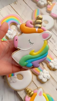 a hand holding a cookie shaped like a unicorn with rainbows and clouds on it