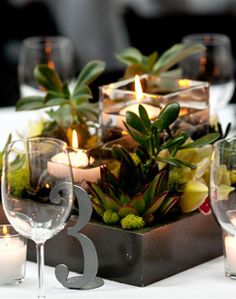 the table is set with wine glasses, candles and succulents