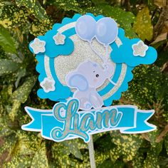 an elephant cake topper on a stick in front of some trees and bushes with leaves