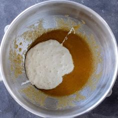 a metal bowl filled with brown liquid and some white substance in it on a gray surface