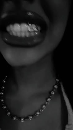 black and white photograph of a woman's mouth with pearls on the chain around her neck