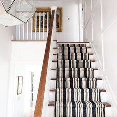 a staircase with black and white striped rugs on the bottom, and a chandelier above it