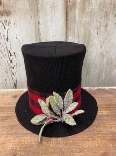 a black top hat with red and green leaves on the brim, sitting on a wooden surface