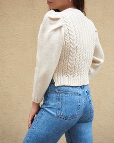 Puff-sleeved crewneck cable knit sweater in cream-colored wool. Features a slightly cropped fit and 3/4 length sleeves. Size Body Length Across Shoulders XS 16.75" 15.5" S 17.75" 16.5" M 18.75" 17.5" L 19.75" 18.5" White Merino Wool Cardigan For Fall, Cream Merino Wool Cardigan For Fall, Cream Wool Cardigan For Fall, Fitted Beige Merino Wool Sweater, Fitted Beige Wool Sweater, Fitted Beige Merino Wool Outerwear, Fitted Long Sleeve Cable Knit Sweater Coat, Cream Wool Sweater For Fall, Fitted Chunky Knit Sweater In Winter White