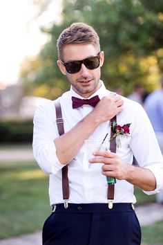 a man wearing sunglasses and suspenders holding a drink