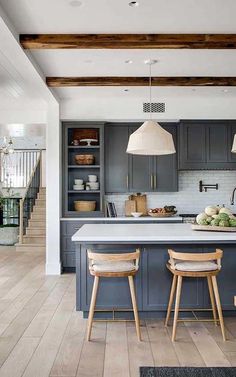 an open kitchen with gray cabinets and white counter tops, two stools in front of the island