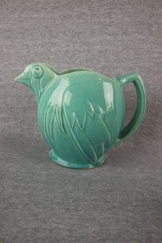 a green ceramic teapot sitting on top of a gray table next to a wall