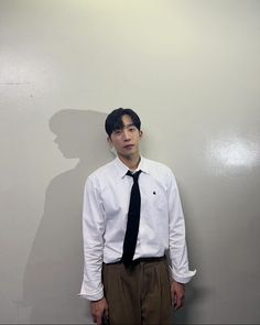 a man standing in front of a wall wearing a black tie and white shirt with his shadow on the wall behind him