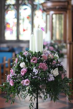 two white candles are sitting on a table with flowers