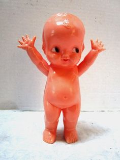 an orange plastic baby doll standing on its hind legs with hands up in the air