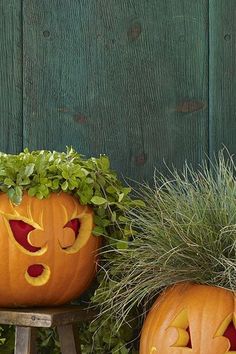 two pumpkins with faces carved into them sitting in front of a wooden fence and planters