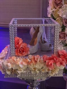 a pair of high heeled shoes sitting on top of a table with flowers around it