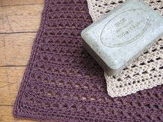 a soap bar sitting on top of a purple crocheted mat next to a white towel