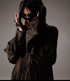 a woman wearing headphones and holding her hands up to her face while standing in front of a gray background