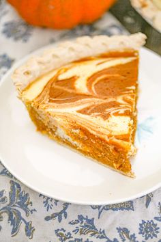 a slice of pumpkin pie on a white plate next to an orange and blue flowered table cloth