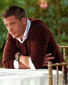 a man sitting at a table with flowers in front of him and looking off to the side