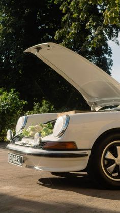 a white car with its hood open sitting on the side of a road next to trees