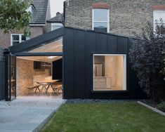 a black house with an open patio and dining table in the back yard, next to a brick building