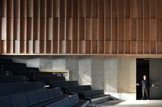 an empty auditorium filled with black seats and wooden slats on the wall behind them