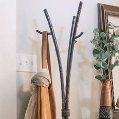 a coat rack with two coats hanging from it's sides next to a potted plant