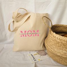 a tote bag sitting next to a woven basket on top of a white sheet