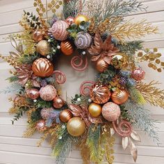 a christmas wreath hanging on the side of a building with ornaments around it and greenery