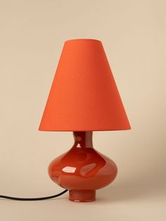 an orange table lamp with a red shade on the base and a black cord plugged into it