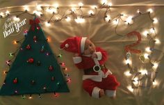 a baby doll laying next to a christmas tree with lights on the wall behind it