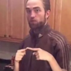 a man holding something in his hand while standing next to a kitchen counter with wooden cabinets