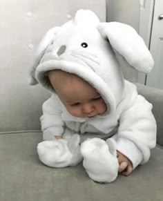 a baby in a white bunny costume sitting on a couch with his legs crossed and head turned to the side