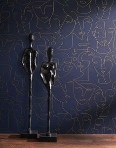 two black sculptures sitting on top of a wooden table in front of a blue wall