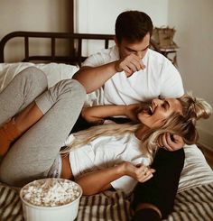 a man and woman laying on top of a bed next to a bowl of popcorn