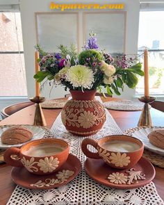 the table is set with two cups and saucers, one has flowers in it