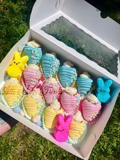 an open box filled with cupcakes on top of a grass covered field next to a person