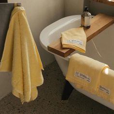 a bath tub sitting next to a window with yellow towels hanging from it's side