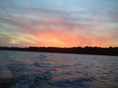 the sun is setting over some water with trees in the background