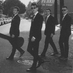 four men in suits and ties walking down the street with their guitar strings hanging out