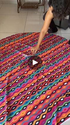 a woman is painting a colorful table cloth on the floor