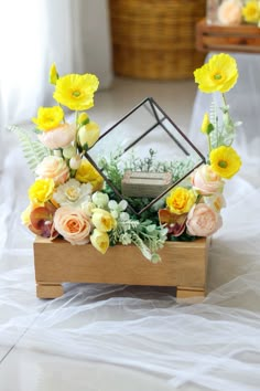 an arrangement of flowers in a wooden box on a white table cloth covered bed sheet