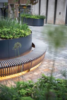 a wooden bench sitting on top of a brick floor next to tall grass and plants