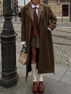 a woman in a coat and tie standing next to a lamp post on the street