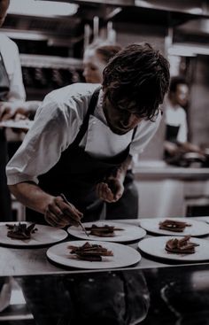 a man in an apron preparing food on top of white plates with utensils