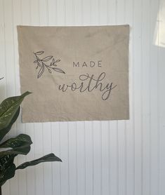 a wall hanging on the side of a building with a plant in front of it